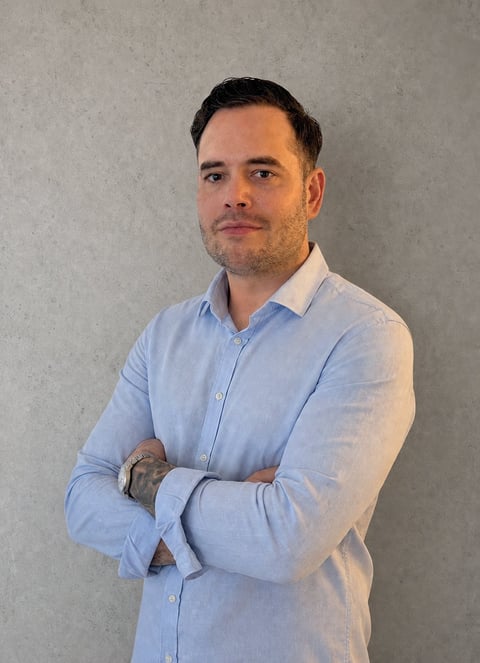 Man in light blue button-up shirt standing with arms crossed against a gray wall, professional portrait